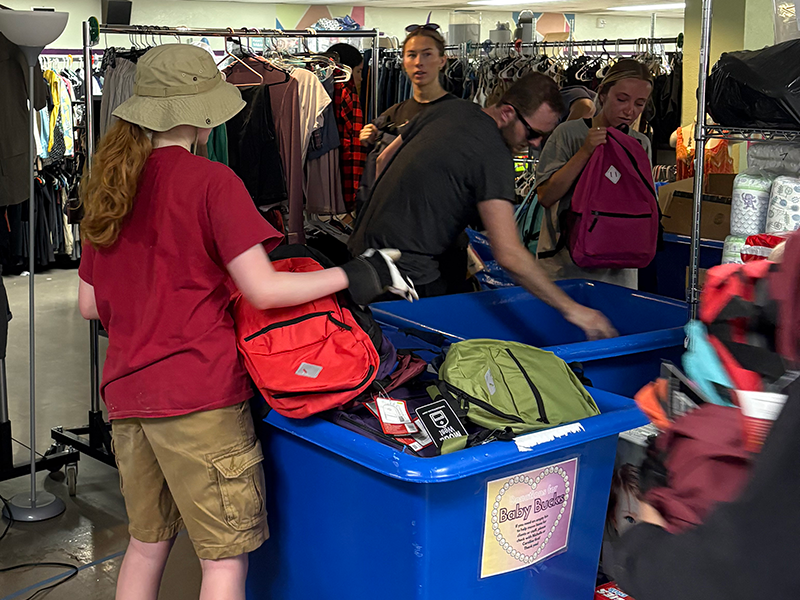 Inset_2025-Day-of-Service_Project-FCS.png students organize backpacks into bins in front of racks of clothing