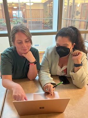 two students seated at table looking at laptop