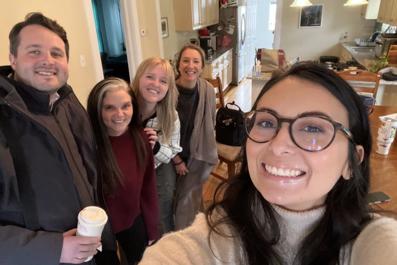 individual taking a selfie with group of four others in a kitchen