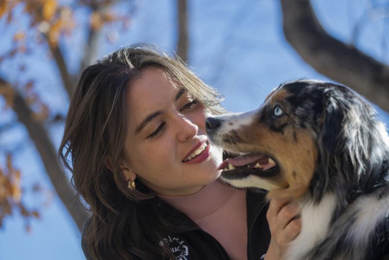 Close-up photo of a woman and a dog's face together as they interact.